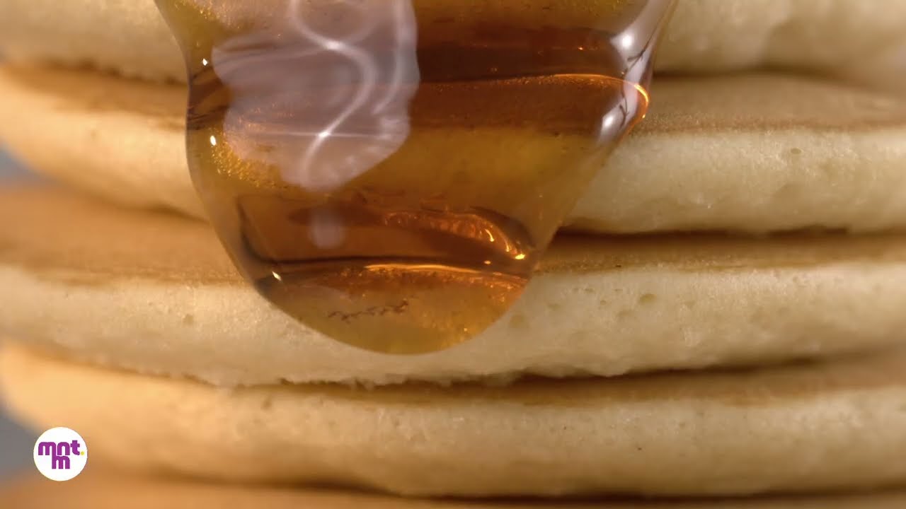 A close-up tabletop frame of honey falling across a stack of pancakes