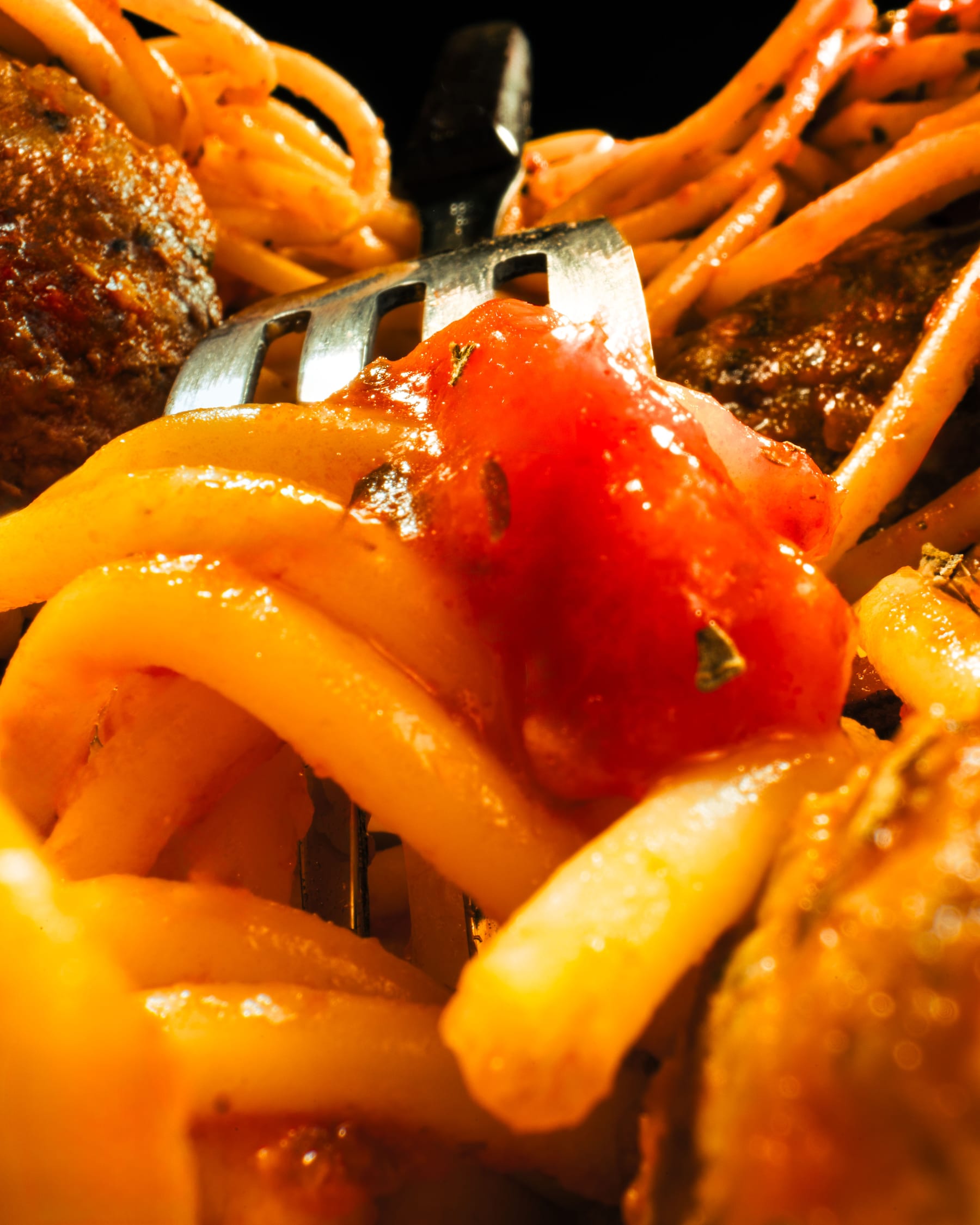 A fork lifting thick pasta ribbons coated in tomato sauce in close macro detail