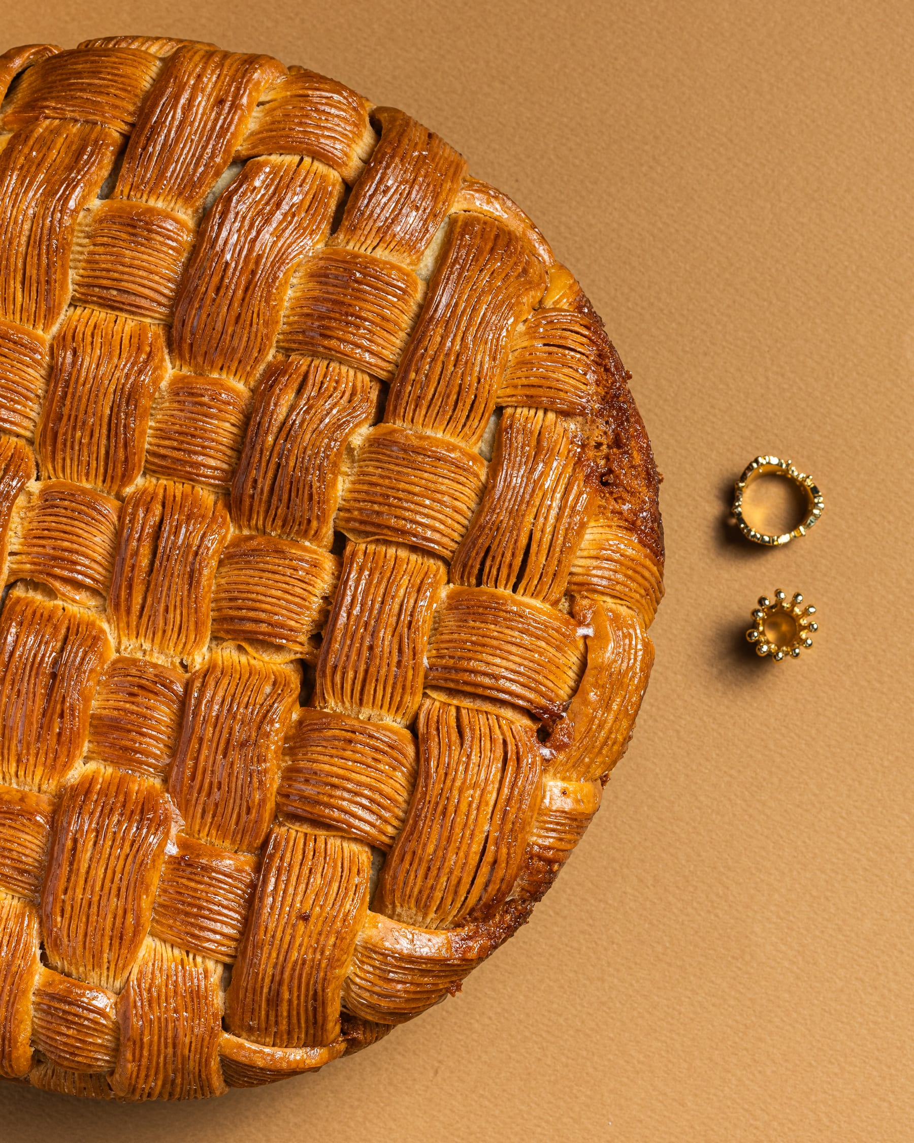 An overhead lattice-topped pie on a tan ground beside two small gold rings