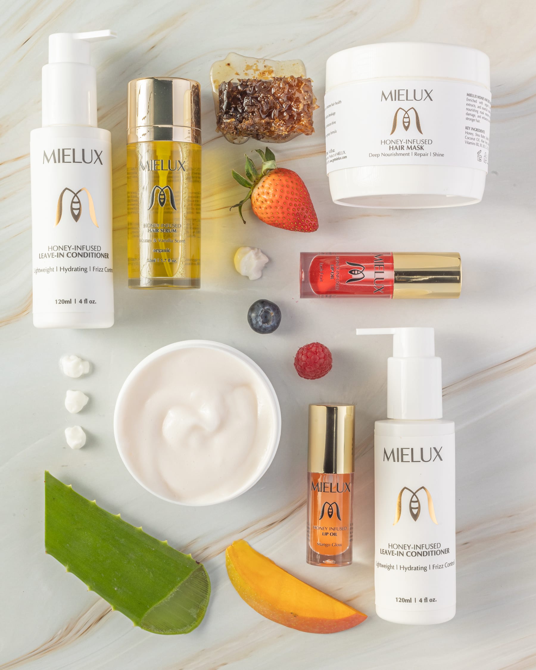 An overhead flat lay of Mielux products with honeycomb, aloe, mango, strawberry, and a bowl of cream