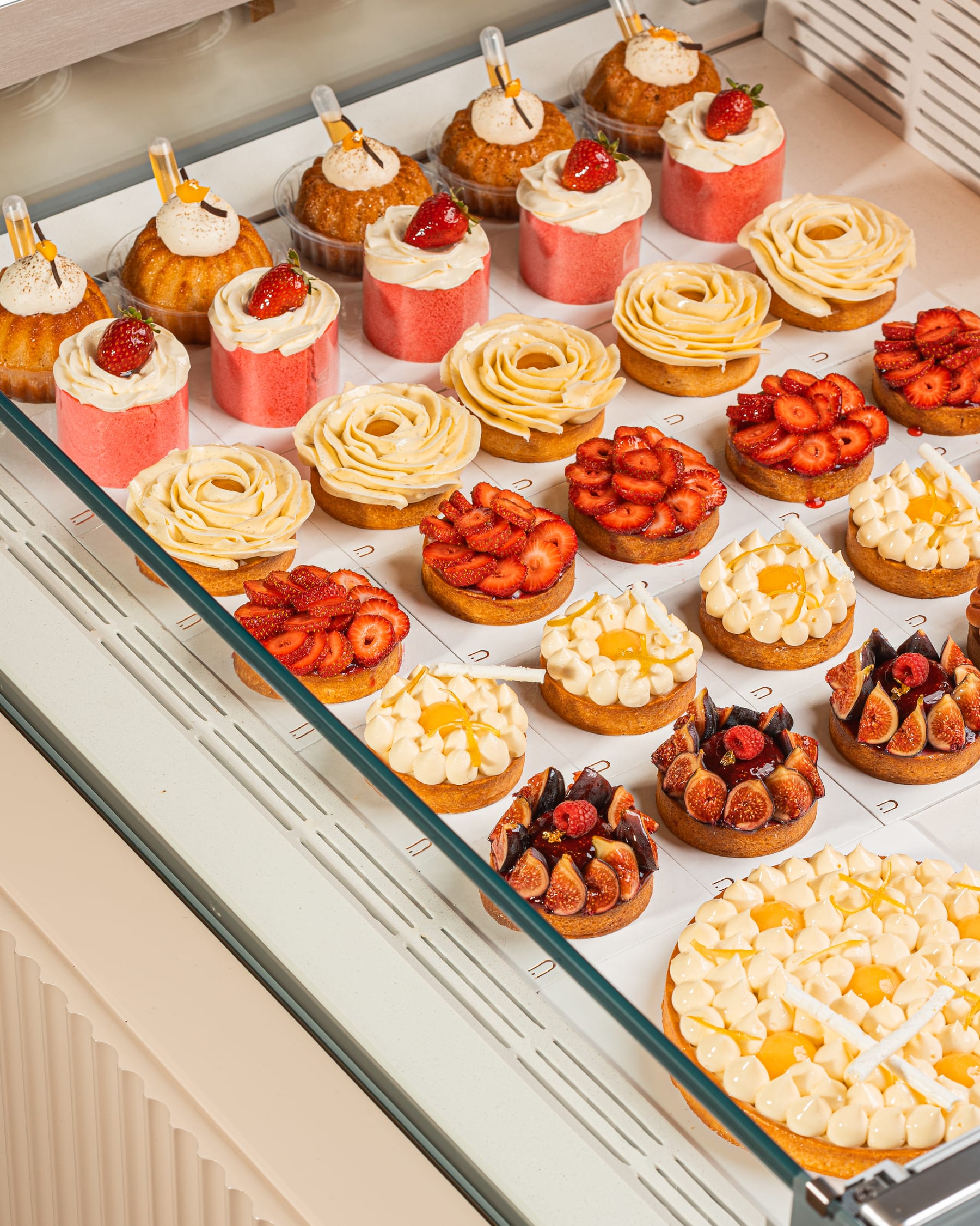 Rows of fruit tarts and cream desserts lined up inside a lit patisserie display case